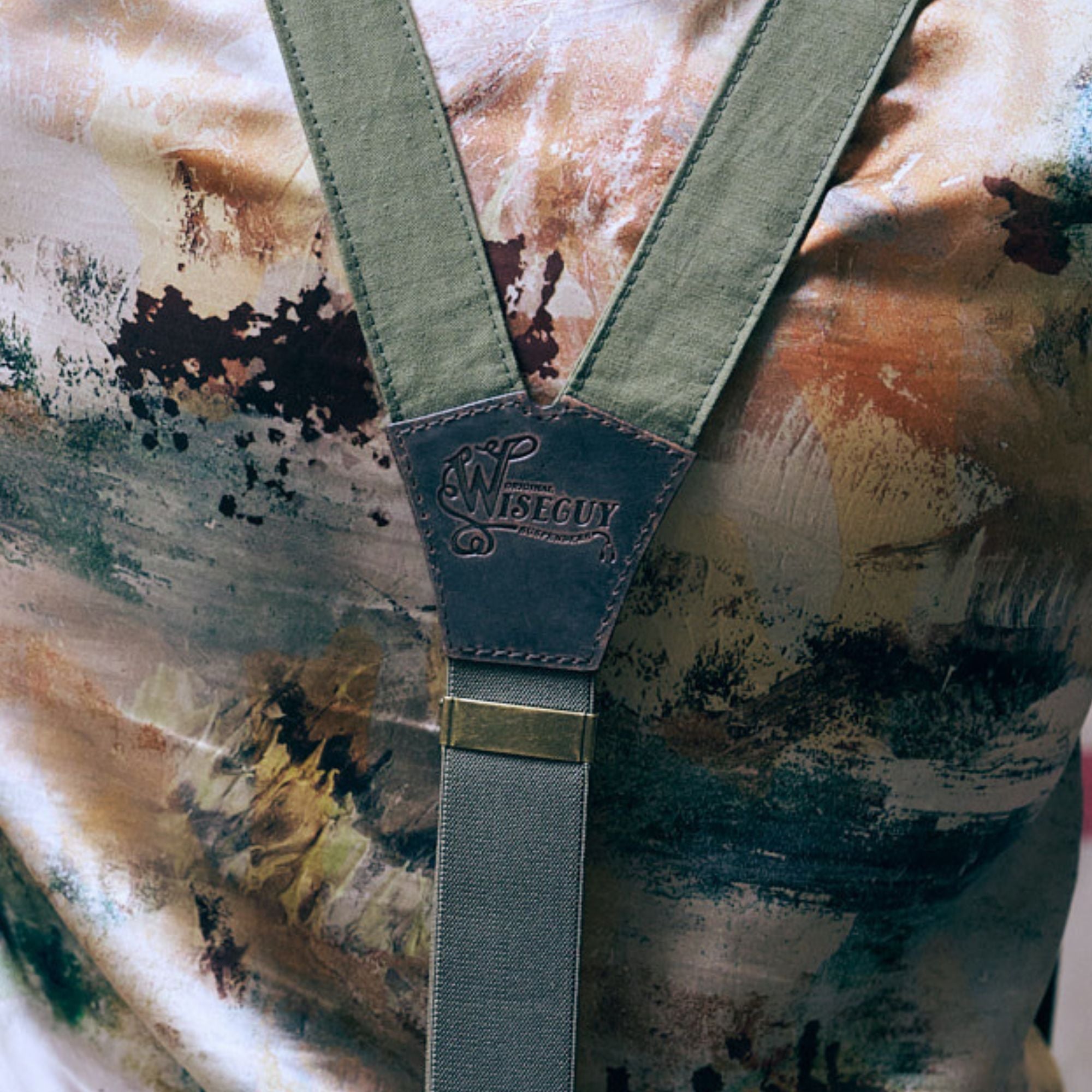 Close up of Army Green Wiseguy Original Suspenders' backpiece. They're worn on top of a camo print shirt.