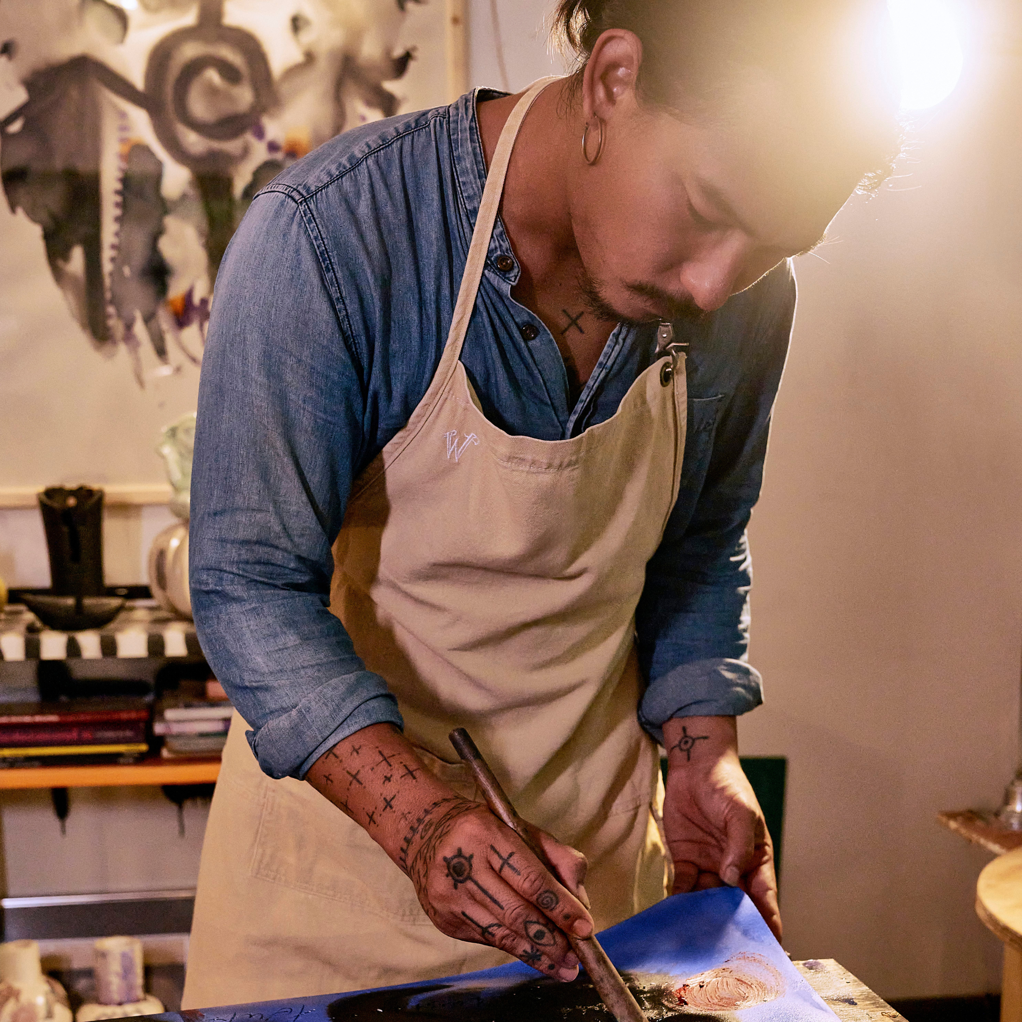 Eakarin in his art studio, he is wearing the Wiseguy Original Apron in the color Beige and is painting.