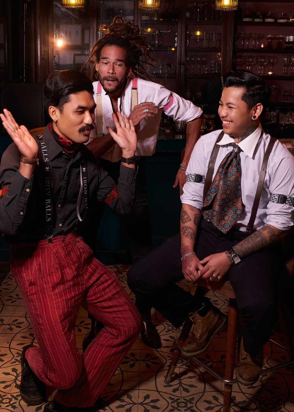 Three man in a bar, two are dancing one is sitting on a bar stool. All of them are wearing Wiseguy Original Suspenders and Sleeve Garters. 